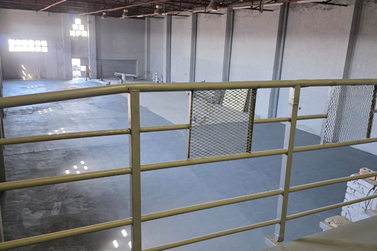 Spacious industrial warehouse interior featuring high ceilings with exposed steel trusses, concrete flooring, and a mezzanine level with metal safety railing.