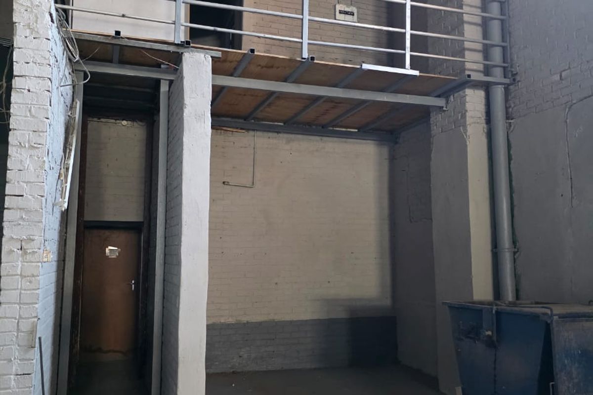 Industrial utility space featuring a mezzanine level with metal railing, exposed brick walls, and concrete flooring, suitable for storage or workshop use.