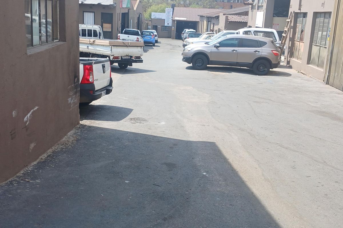 Rear industrial yard area featuring asphalt paving, access to multiple warehouse units with roller shutter doors, and exterior wall surfaces.