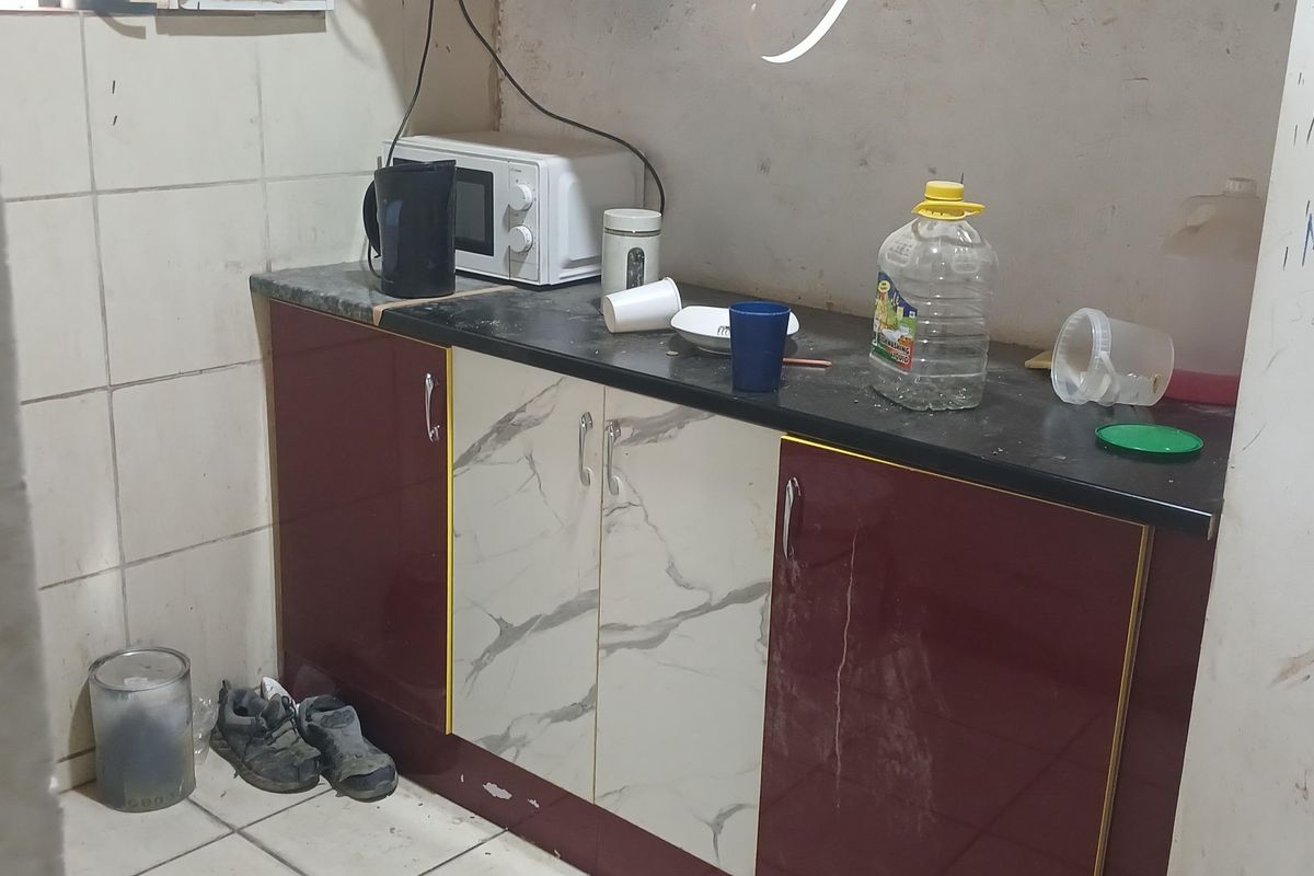 A compact kitchen area featuring two-tone cabinetry, stone-look laminate countertops, and tiled wall finishes, currently showing signs of wear and surface damage.