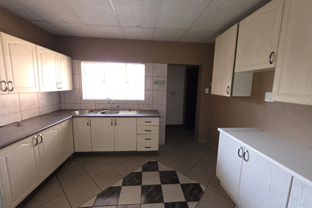 A functional kitchen area featuring light-toned cabinetry, laminate countertops, a double sink, and tiled flooring with a decorative central inlay.