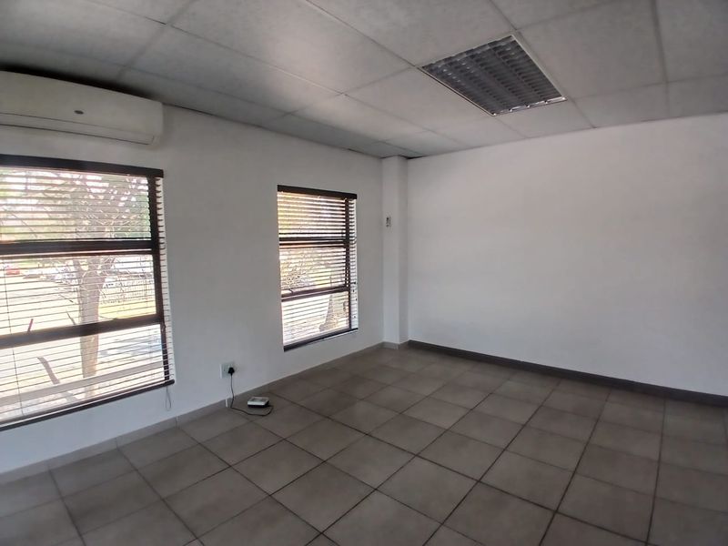 A vacant office space featuring tiled flooring, a suspended ceiling with recessed lighting, and a wall-mounted air conditioning unit.
