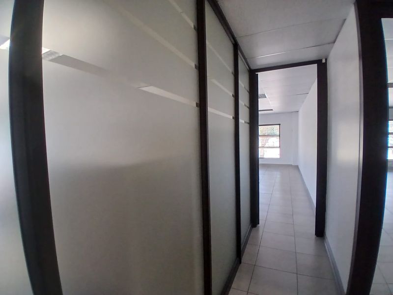 A bright, modern office hallway featuring frosted glass partitions, tiled flooring, and a clean, minimalist aesthetic suitable for a professional workspace.
