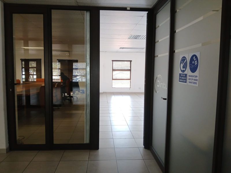 A bright, vacant office space featuring tiled flooring, a suspended ceiling, and glass partition doors leading to an adjacent meeting area.
