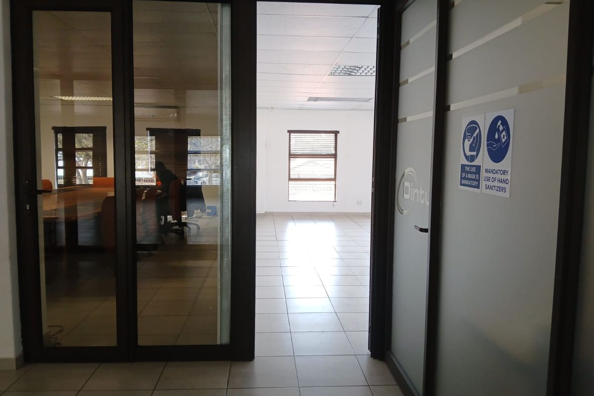 A bright, vacant office space featuring tiled flooring, a suspended ceiling, and glass partition doors leading to an adjacent meeting area.