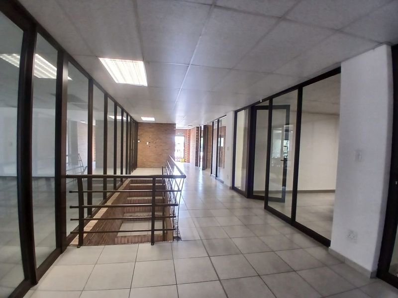 Spacious office hallway featuring tiled flooring, glass partition walls, and a modern suspended ceiling with recessed lighting.