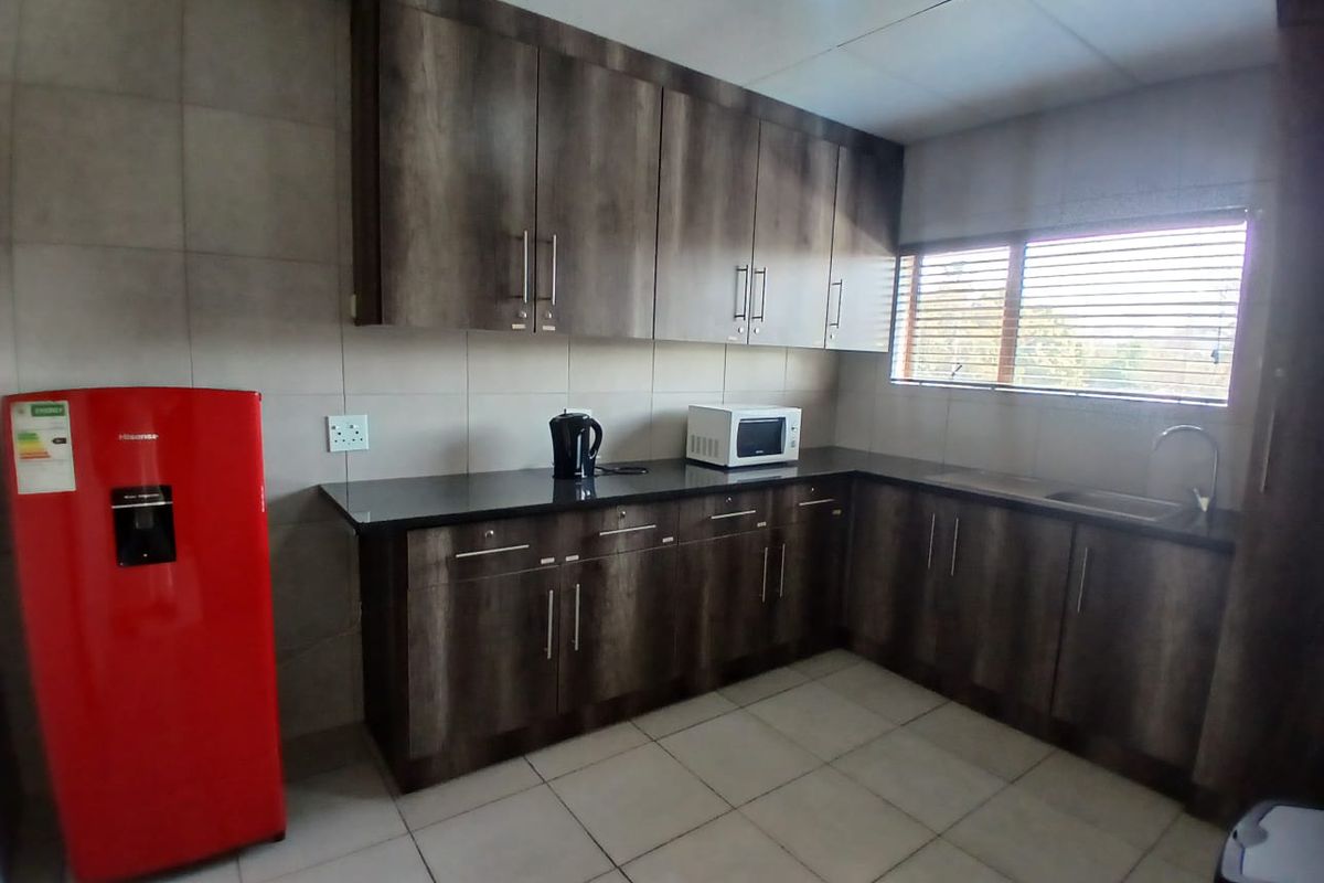A functional office kitchenette featuring dark wood-grain cabinetry, granite countertops, a stainless steel sink, and neutral tiled flooring.