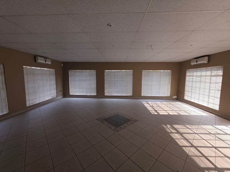 Spacious, open-plan office area featuring tiled flooring, multiple windows with fitted blinds, and wall-mounted air conditioning units.