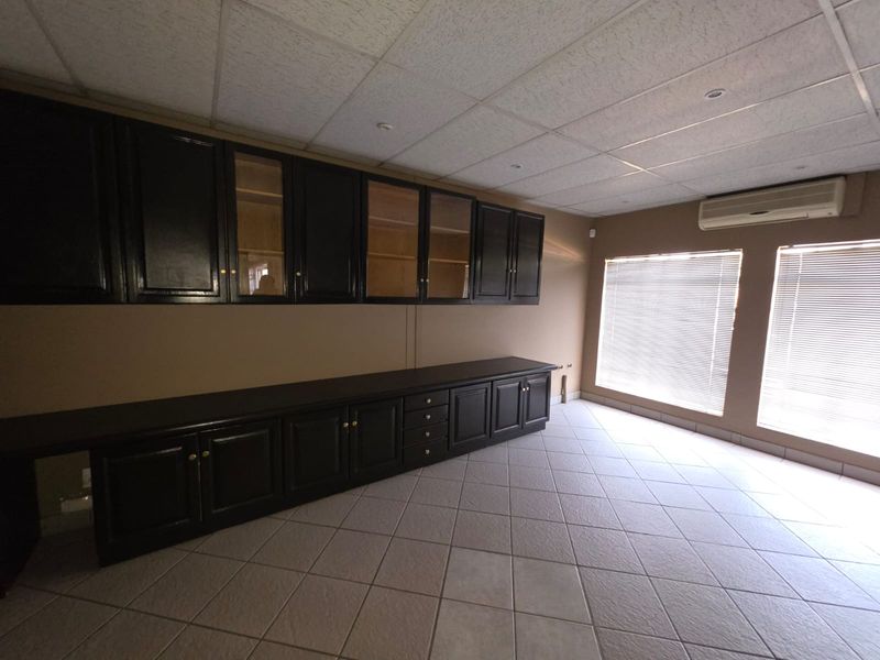 Spacious office area featuring extensive built-in dark wood cabinetry, tiled flooring, recessed lighting, and wall-mounted air conditioning unit.