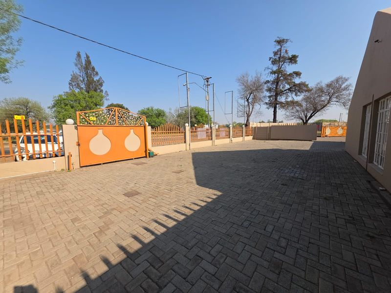 A paved exterior parking area featuring a secure perimeter wall with decorative metal fencing and a large orange sliding gate.