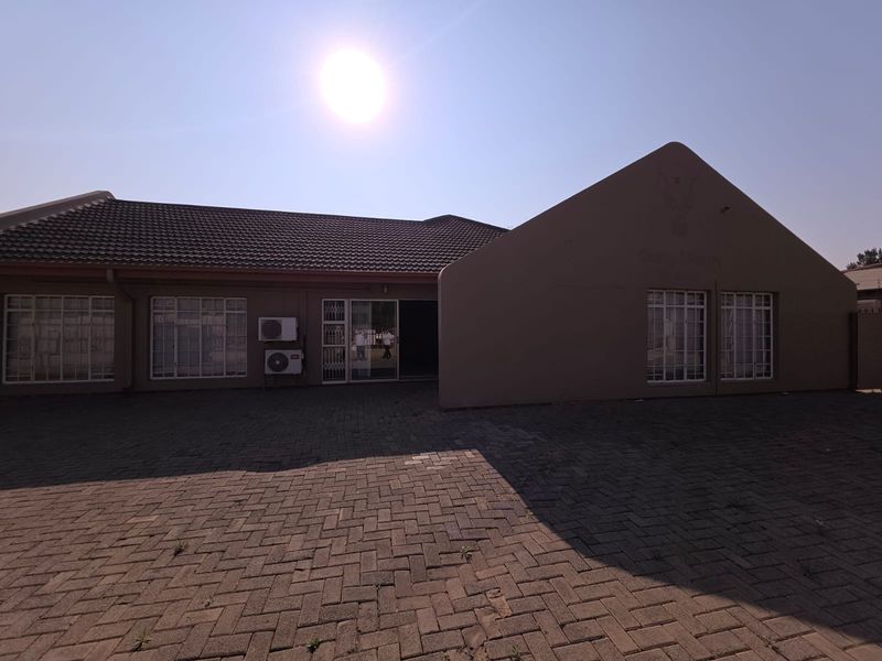 Exterior view of the office building featuring a paved courtyard, tiled roof, and security-barred windows.