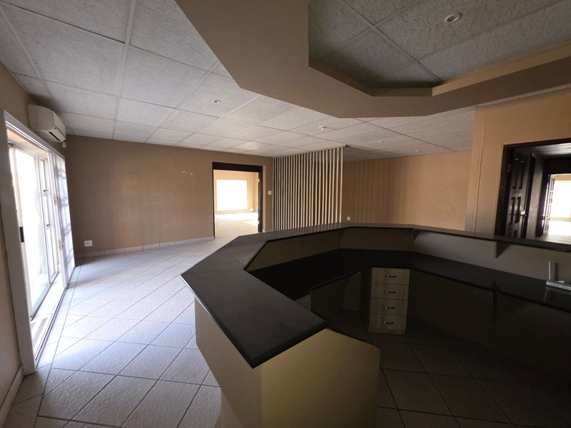 Spacious office reception area featuring a built-in service counter, tiled flooring, suspended ceiling, and sliding glass door access.
