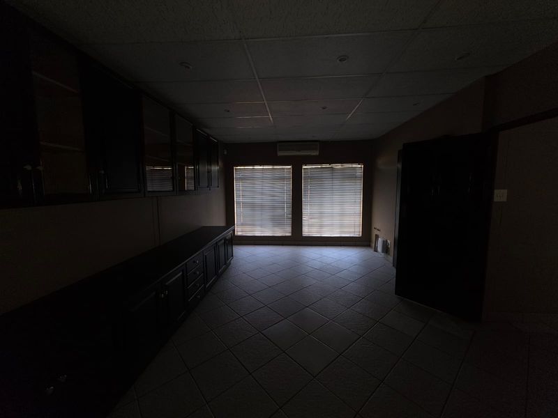 An office space featuring built-in dark cabinetry, tiled flooring, a drop ceiling, and a wall-mounted air conditioning unit.