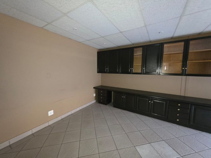 A functional office space featuring built-in dark cabinetry, tiled flooring, and a suspended acoustic ceiling grid.