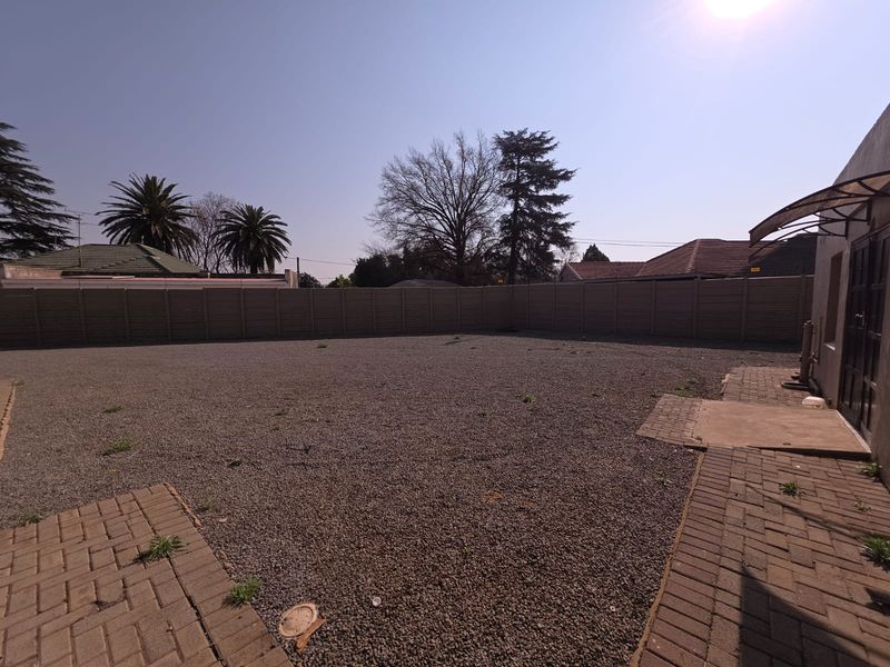 A spacious, low-maintenance rear courtyard featuring gravel surfacing, paved walkways, and perimeter walling, suitable for outdoor office use or parking.