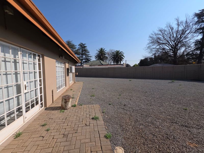 A view of the rear exterior area featuring paved patio space, gravel ground cover, and perimeter walling.