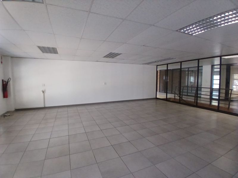 An open-plan office space featuring tiled flooring, a suspended ceiling with recessed lighting, and a glass partition wall.