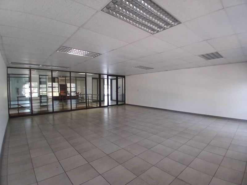 Spacious, empty office area featuring a suspended ceiling with recessed lighting, tiled flooring, and a glass partition wall providing a professional, open layout.