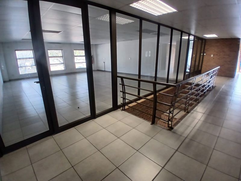 Spacious open-plan office area featuring glass partitions, tiled flooring, and a modern staircase, offering a bright and professional workspace environment.