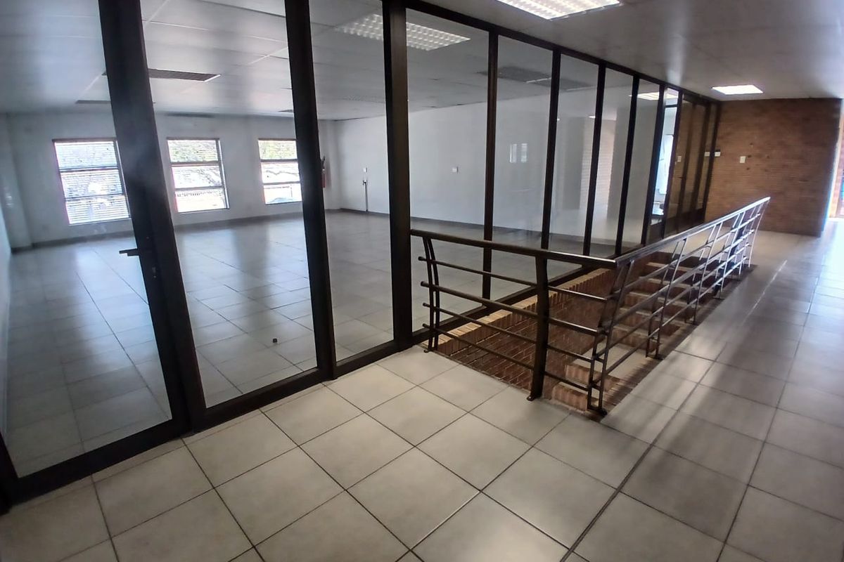 Spacious open-plan office area featuring glass partitions, tiled flooring, and a modern staircase, offering a bright and professional workspace environment.
