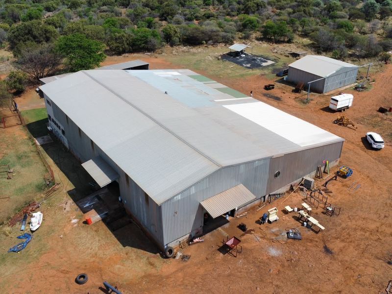 Aerial view of a large industrial-style farm shed with metal roofing, surrounded by open land and additional outbuildings.