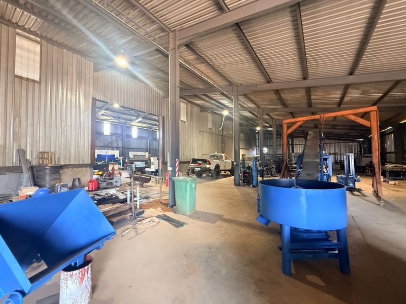 Spacious industrial utility shed featuring a steel frame structure, corrugated metal walls, and concrete flooring, suitable for workshop or storage operations.