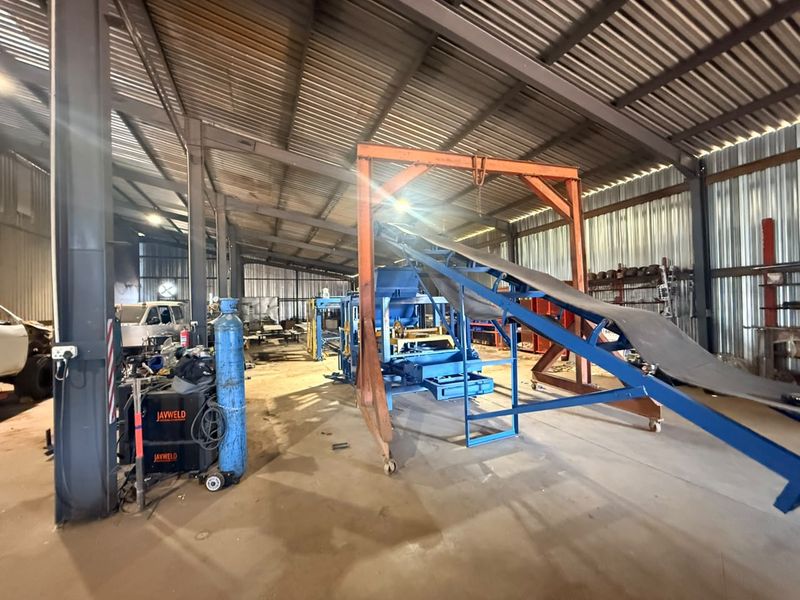 A large industrial utility space or workshop featuring a steel portal frame, corrugated metal cladding, and heavy-duty machinery including a conveyor system.