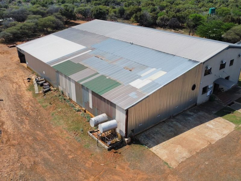 Aerial view of a large farm shed featuring corrugated metal roofing, external water tanks, and a concrete apron area.