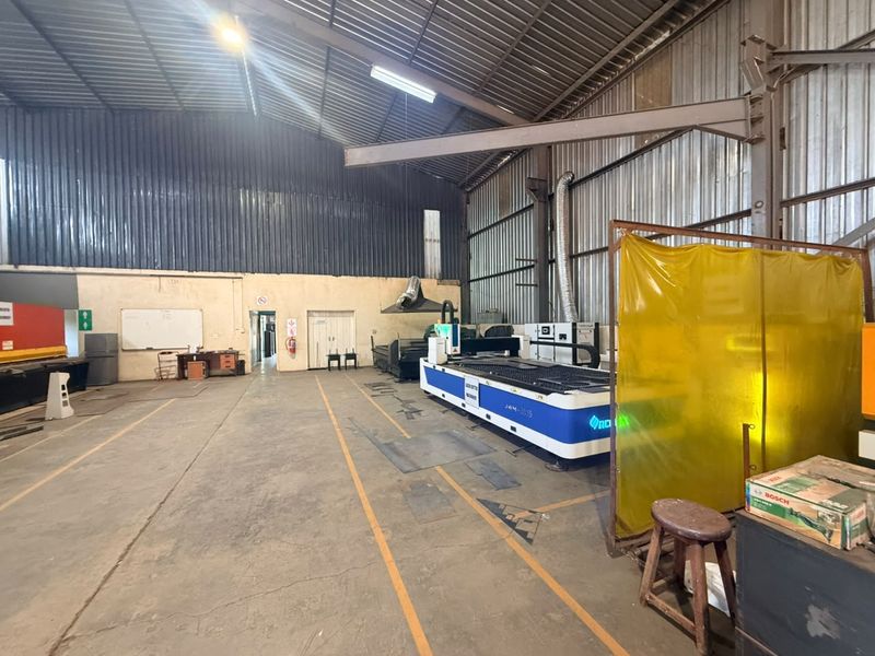 A functional industrial utility space featuring high-clearance corrugated metal roofing, concrete flooring, and integrated ventilation systems suitable for workshop or manufacturing operations.