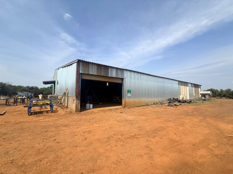 A large industrial-style utility shed or workshop featuring corrugated metal cladding and a wide roller shutter entrance on a rural farm property.