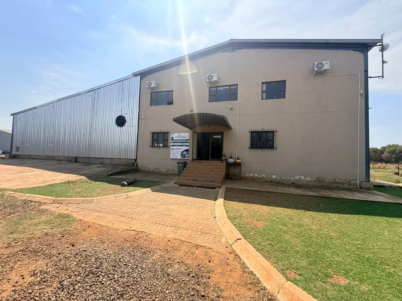 Front elevation of a large industrial-style farm building featuring corrugated metal siding, plastered walls, and a paved entrance area.
