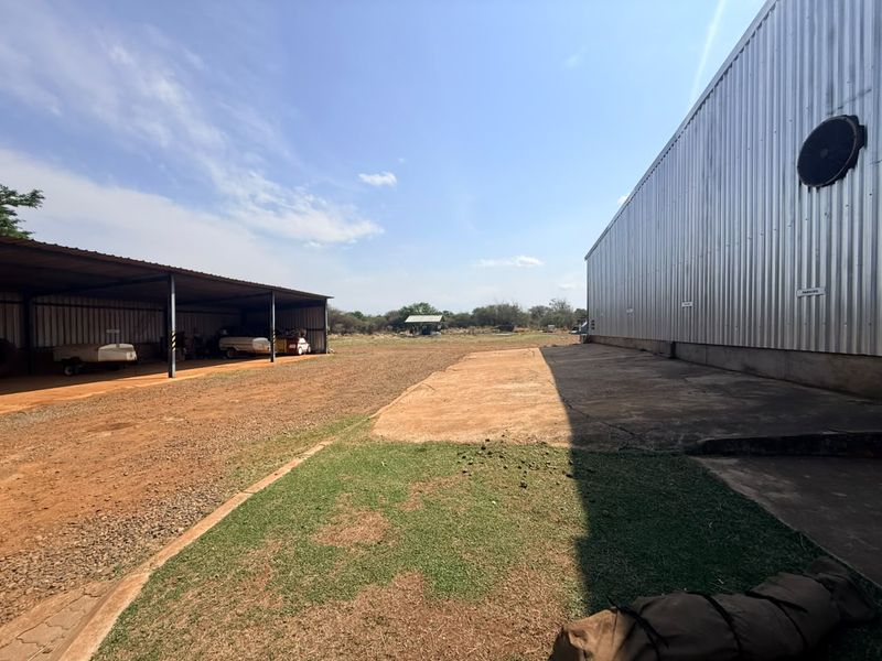 Spacious farm yard area featuring a large corrugated metal shed, an open-sided carport structure, and a concrete apron with surrounding gravel and grass.