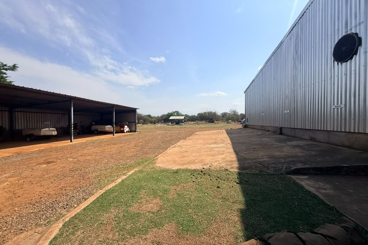 Spacious farm yard area featuring a large corrugated metal shed, an open-sided carport structure, and a concrete apron with surrounding gravel and grass.