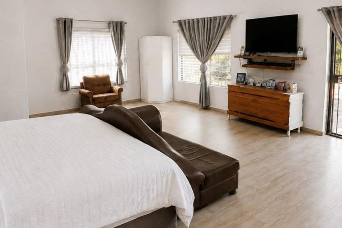 Spacious bedroom featuring light-toned tiled flooring, large windows with curtains, and direct access to the exterior through a security gate.