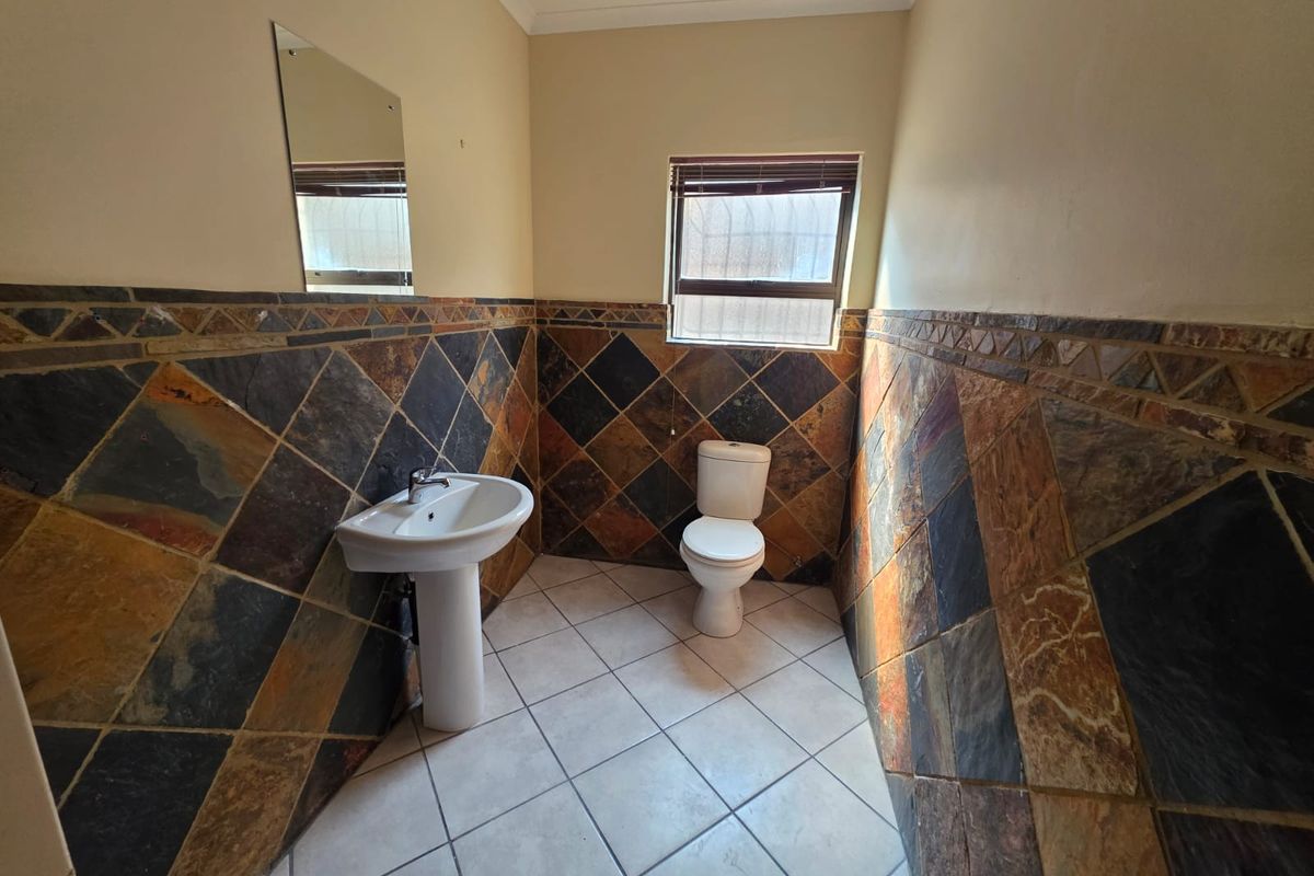 A functional bathroom featuring a pedestal basin, toilet, and decorative slate-style wall tiling with a window for natural light.