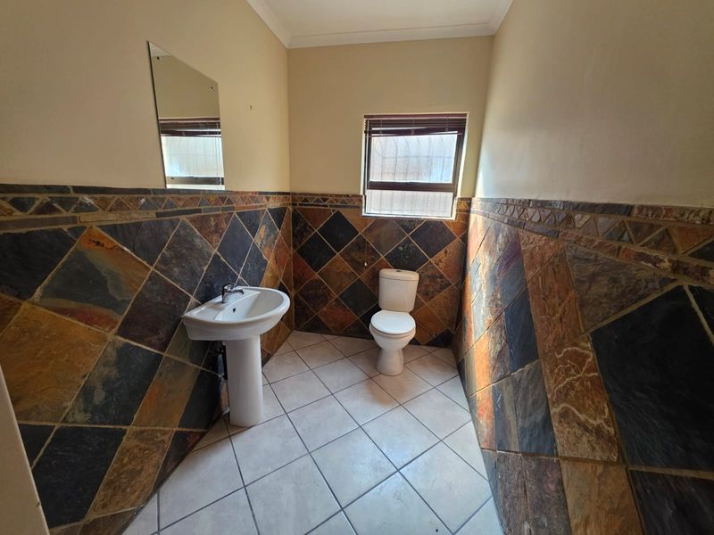 A functional bathroom featuring a pedestal basin, toilet, and decorative slate-style wall tiling with a window for natural light.