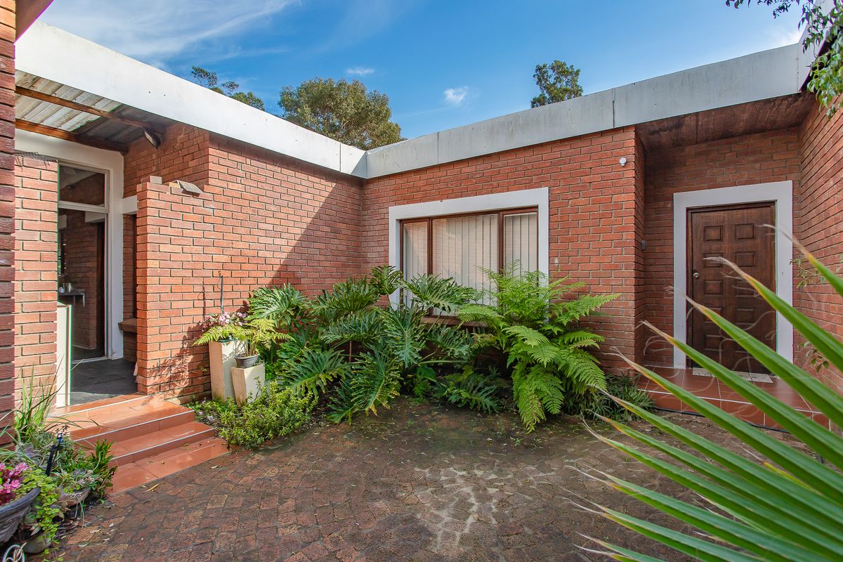 A private brick-walled courtyard featuring paved flooring, tiled entrance steps, and established garden beds, providing a secluded outdoor space.