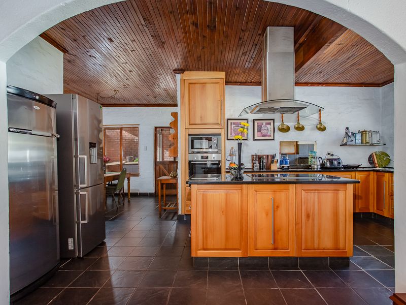 A spacious kitchen featuring a wooden tongue and groove ceiling, a central island with granite countertops, and built-in stainless steel appliances.