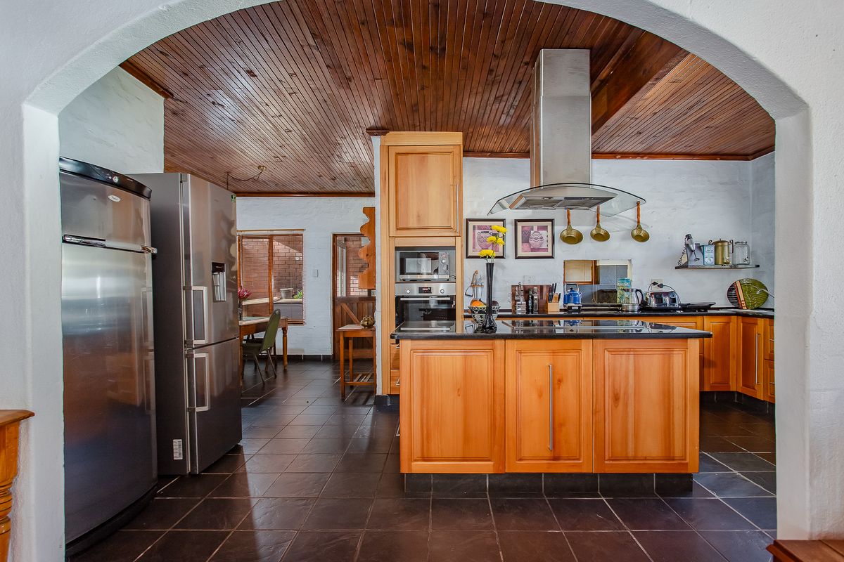 A spacious kitchen featuring a wooden tongue and groove ceiling, a central island with granite countertops, and built-in stainless steel appliances.