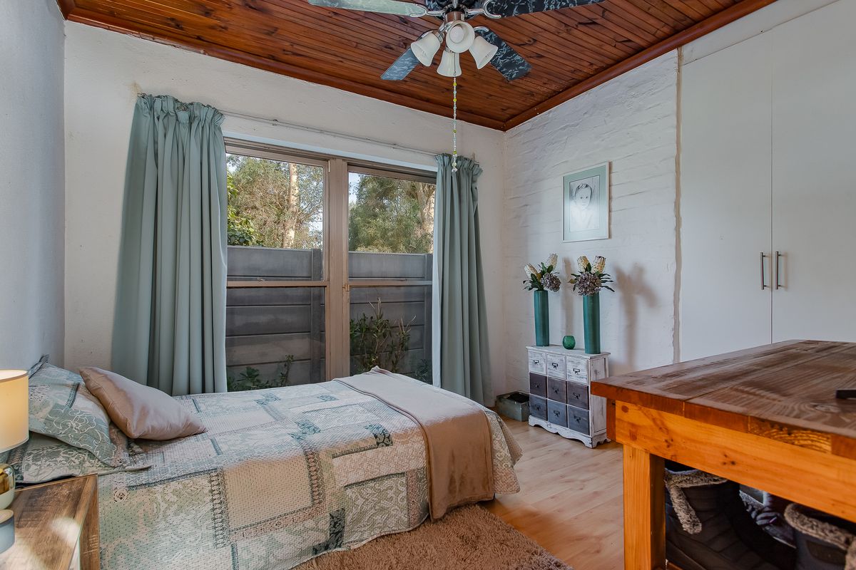 A cozy bedroom featuring a timber ceiling, ceiling fan, built-in wardrobe, and laminate flooring, with a view of the exterior through the window.