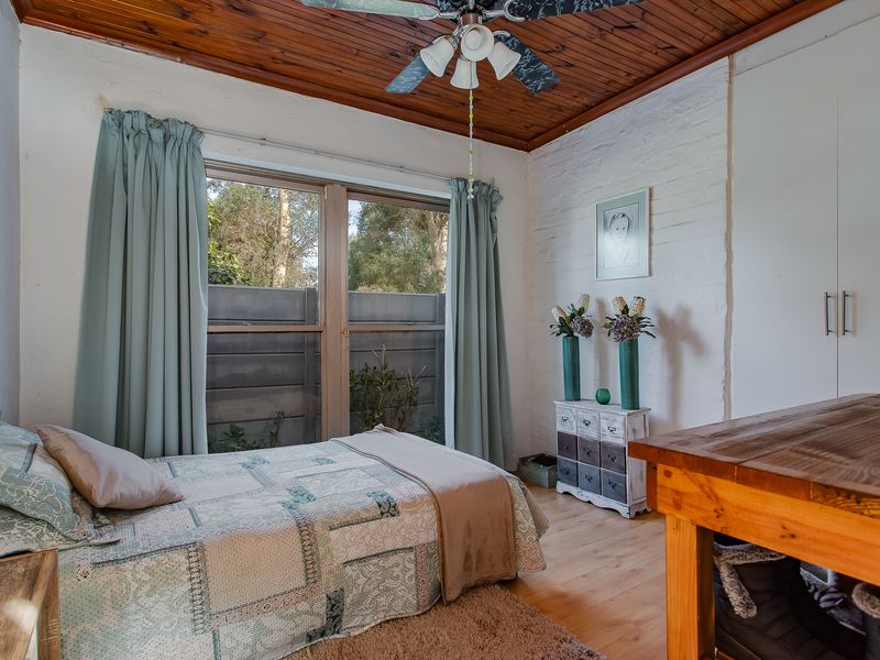 A cozy bedroom featuring a timber ceiling, ceiling fan, built-in wardrobe, and laminate flooring, with a view of the exterior through the window.