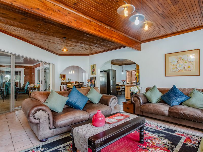 Spacious open-plan living area featuring a vaulted timber-clad ceiling with exposed beams, ceramic tiled flooring, and arched transitions to the kitchen and dining spaces.