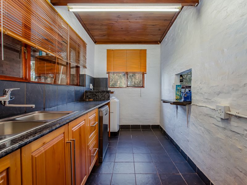 Functional scullery featuring wooden cabinetry, granite countertops, double stainless steel sink, and tiled flooring with a timber-clad ceiling.