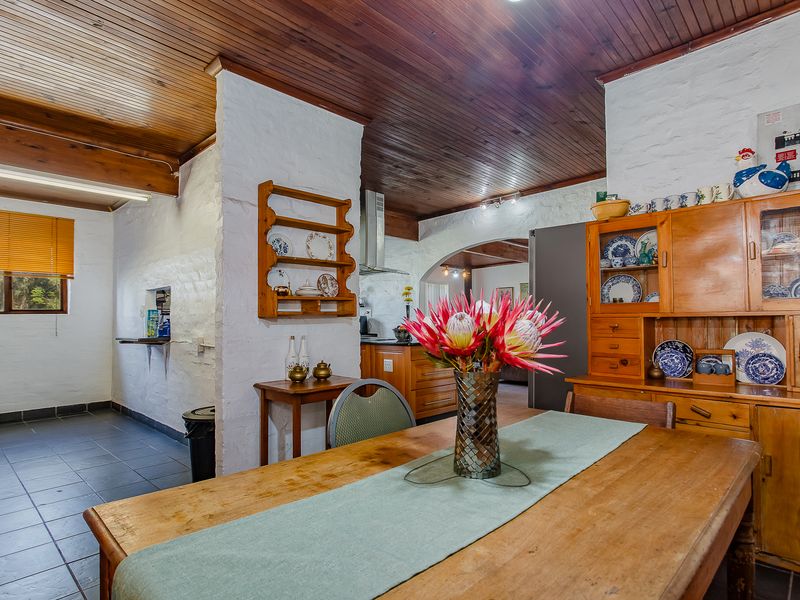 Open plan kitchen and dining area featuring rustic painted brick walls, timber tongue and groove ceilings, and tiled flooring with integrated cabinetry.