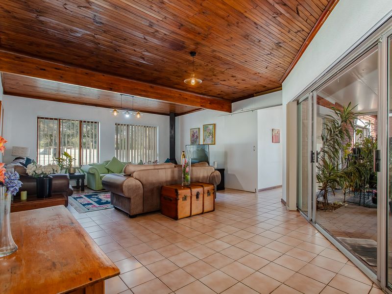 Spacious living room featuring a vaulted timber ceiling with exposed beams, ceramic tiled flooring, and large sliding glass doors leading to an outdoor area.