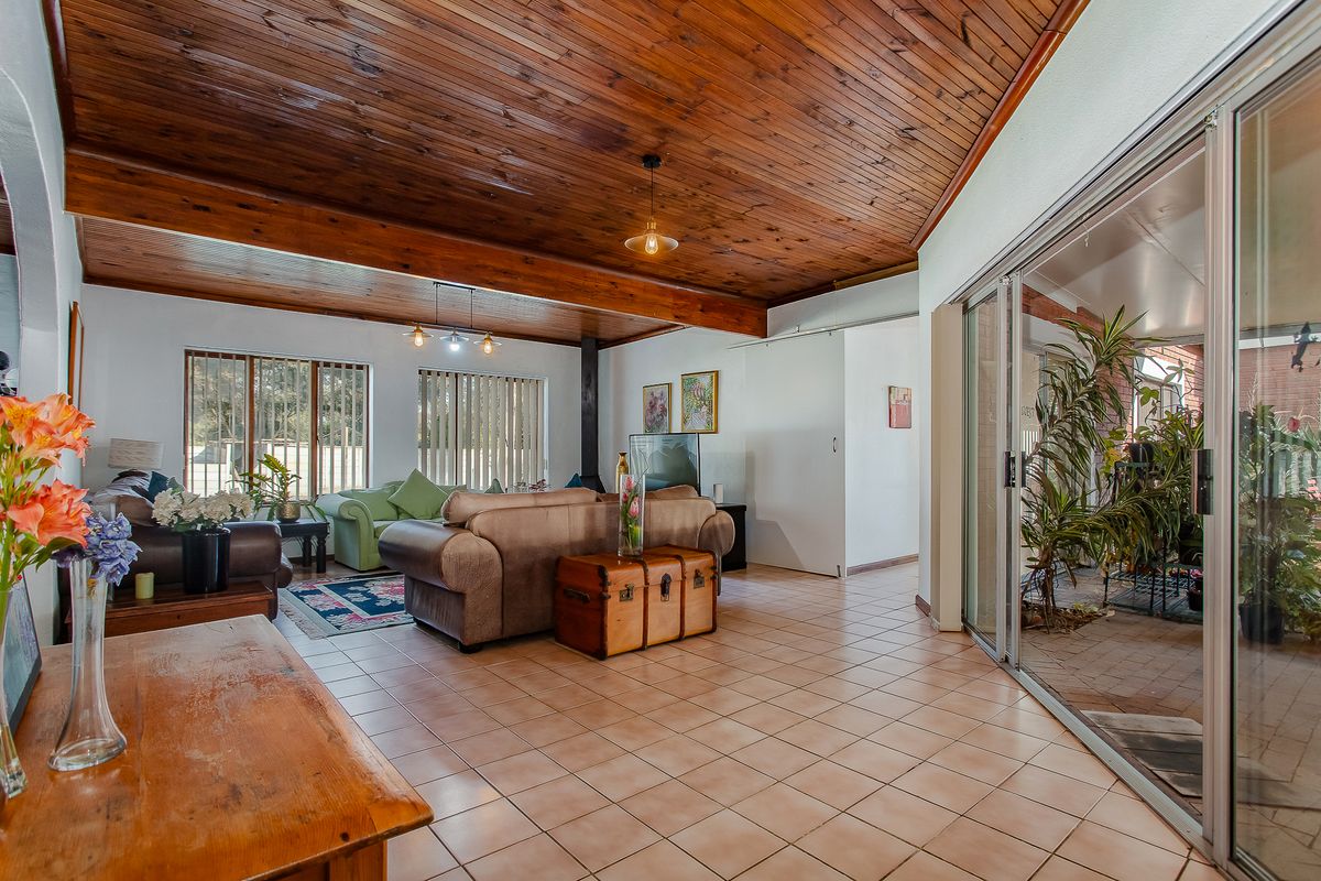 Spacious living room featuring a vaulted timber ceiling with exposed beams, ceramic tiled flooring, and large sliding glass doors leading to an outdoor area.