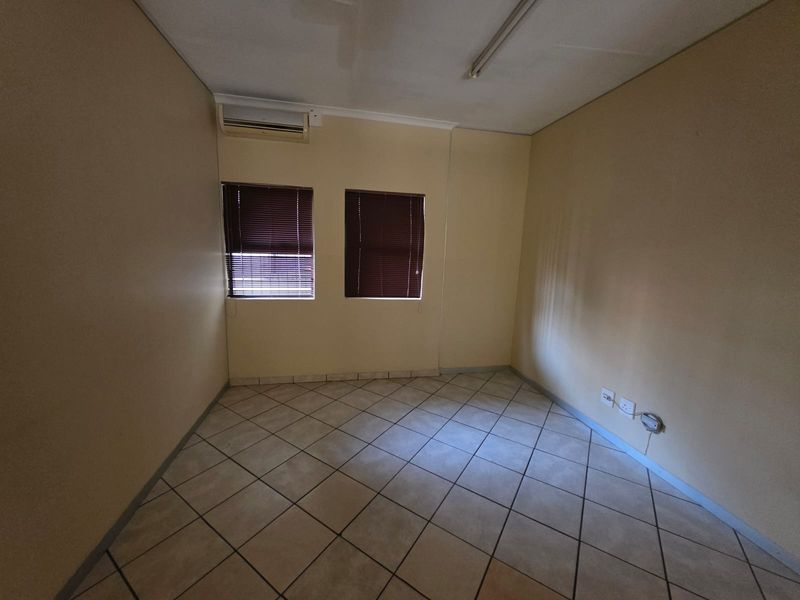 A vacant office space featuring tiled flooring, dual windows with blinds, and a wall-mounted air conditioning unit.