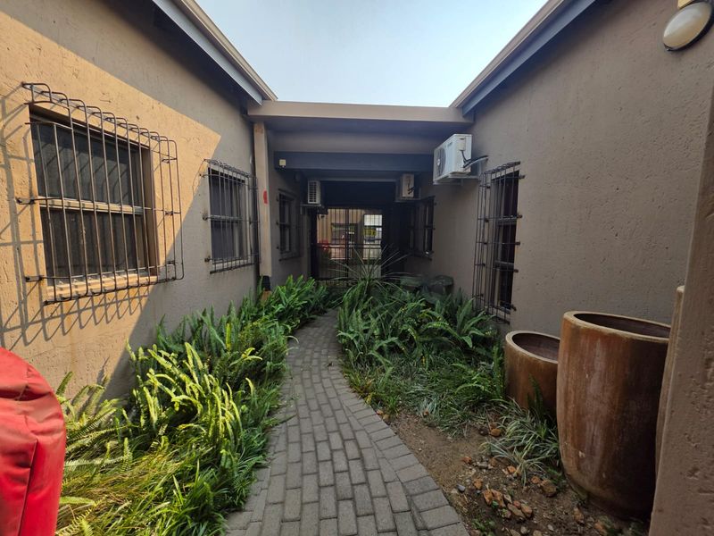 A paved walkway leads between two building wings, featuring landscaped garden beds, security bars on windows, and wall-mounted air conditioning units.