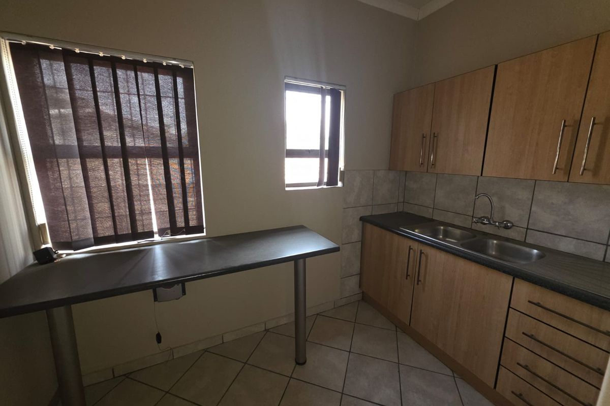 Functional kitchen area featuring wood-look cabinetry, double basin sink, tiled splashback, and a built-in breakfast counter with tiled flooring.