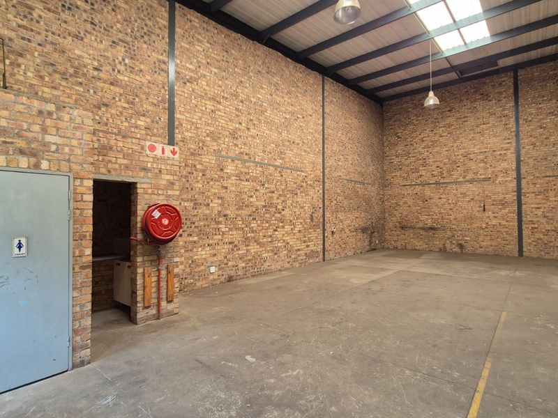 Spacious industrial warehouse unit featuring exposed brick walls, concrete flooring, high ceilings with skylights, and an integrated fire hose reel.